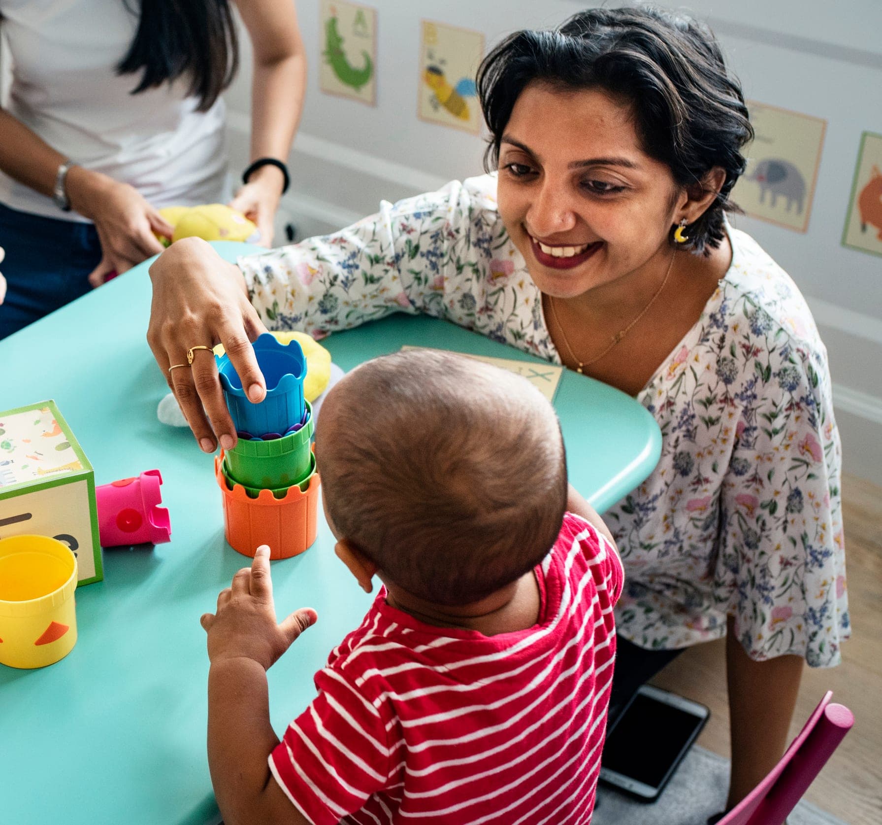 A Morgan’s Early Learning Centers teacher smiling with a toddler stacking colorful cups at a classroom table